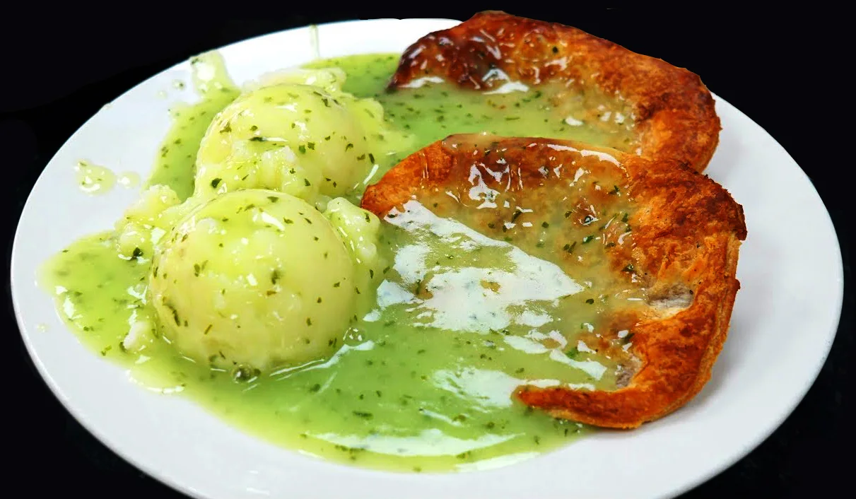 A plate of pie, mash and liquor: two pieces of golden pastry pie, two scoops of mash, and green parsley liquor poured over.